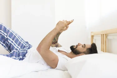 Relaxed man lying on bed using cellphone
